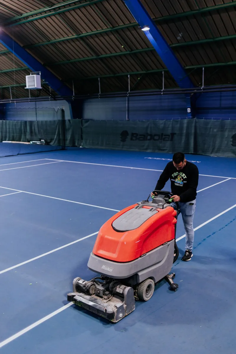 Employé de Pro-Net nettoyant un court de tennis intérieur avec une autolaveuse à Paris.