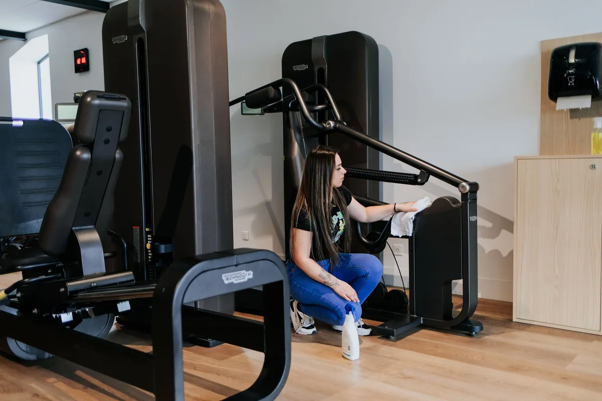 Employée de Pro-Net nettoyant une machine de musculation dans une salle de sport à Paris