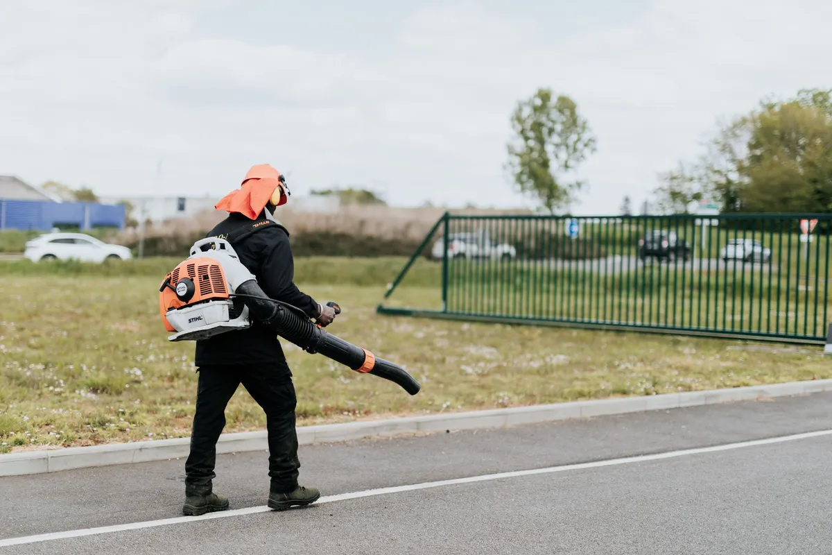 Employé de Pro-Net utilisant un souffleur de feuilles pour nettoyer un espace extérieur.