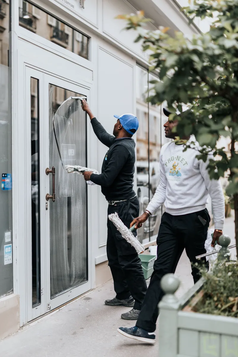 Deux employés de Pro-Net nettoyant la vitrine d'un magasin à Paris, équipés de matériel professionnel.