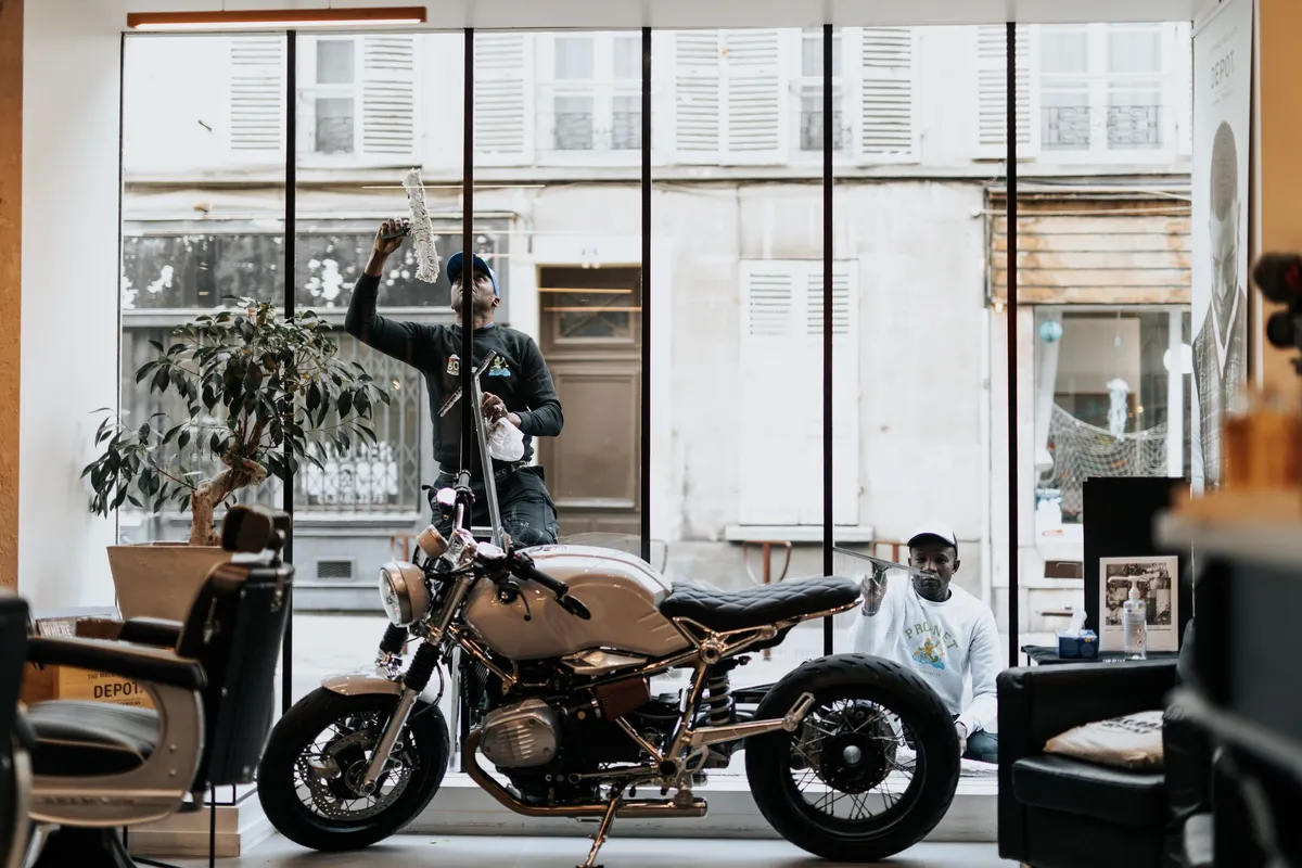 Deux employés de Pro-Net nettoyant les vitres d'un magasin avec une moto exposée à l'intérieur à Paris.