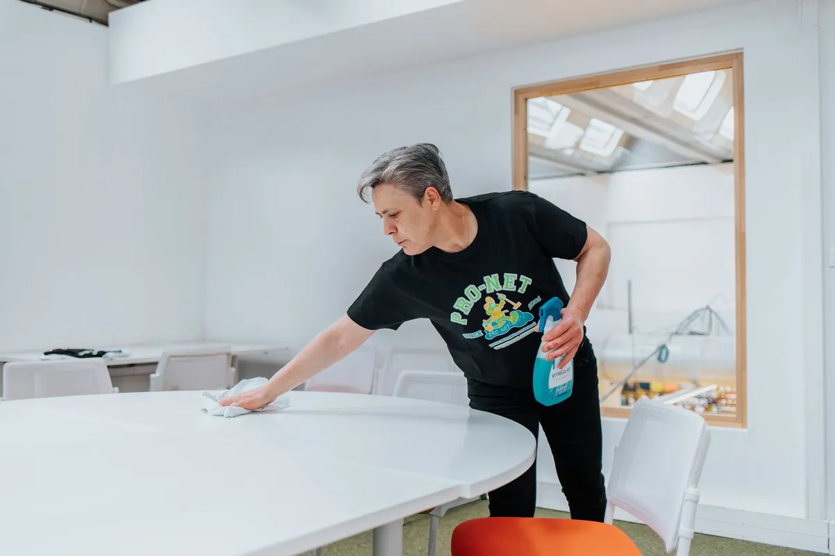 Employé Pro-Net nettoyant une table de réunion dans une salle lumineuse à Paris.