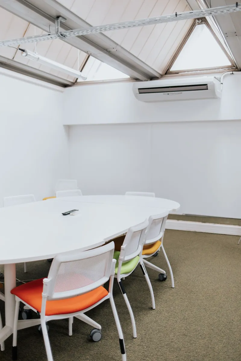 Salle de réunion moderne avec table blanche et chaises colorées sous un plafond incliné avec fenêtres à Paris.